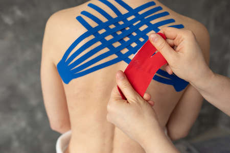 Closeup cropped doctor, physiotherapist hands taping blue, red stripes on back muscles for...