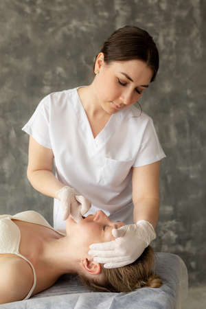 Vertical woman physiotherapist, osteopath doing anti wrinkle manual myofascial face massage by...