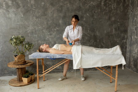 Concentrated female medical therapist applying cupping bubble massage to relaxing patient stomach....