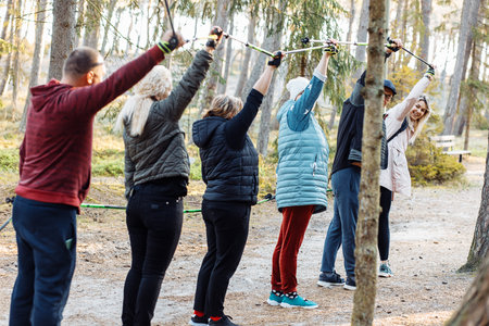 Senior people with female coach leader hold Nordic trekking sticks in air while hiking in the...
