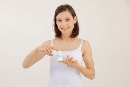 Young smiling woman advertising useful vitamins for women closeup, white background. Holding in...