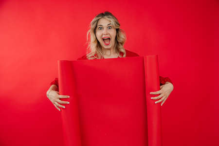 Portrait of funny crazy woman with bright makeup uncovering red empty whatman paper isolated on red background. Marketing and advertisement, free copy space. Fashion and beauty industryの写真素材