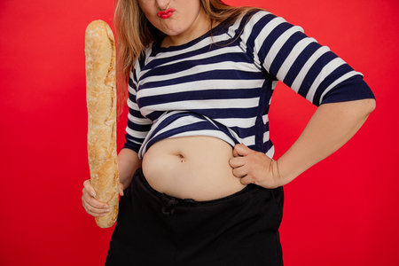 Unrecognizable overweight fat plump woman in striped shirt holding french bread baguette and naked...