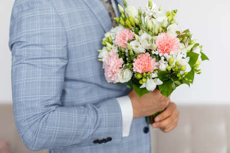 Cropped photo of man groom fiance wearing blue stylish checkered suit, holding bridal bouquet of pink and white flowers.の写真素材