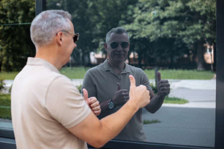 Portrait back view of senior smiling man in sunglasses walking on street along modern office...