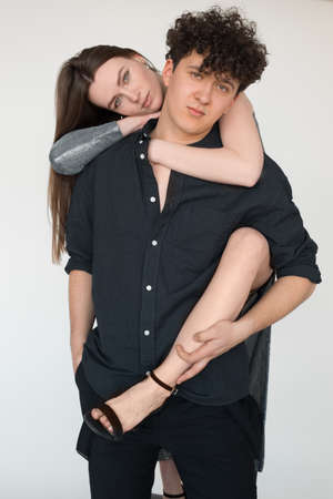 Portrait closeup of beautiful loving couple in festive outfits, gray studio background. Attractive young girl lying on shoulders of cute boyfriend and gently embracing. Love and feelingsの写真素材
