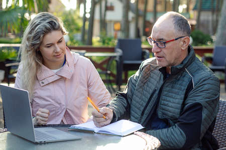 Portrait of serious middle-aged man father writing notes, listening to young woman, discussing information in cafe.の写真素材