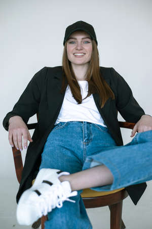 Portrait of smiling girl sitting on chair, gray studio background, copy space. Female casual black...