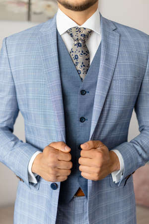 Cropped photo of man groom wearing blue stylish checkered suit, vest, white shirt, grey tie, holding jacket with hands.の写真素材