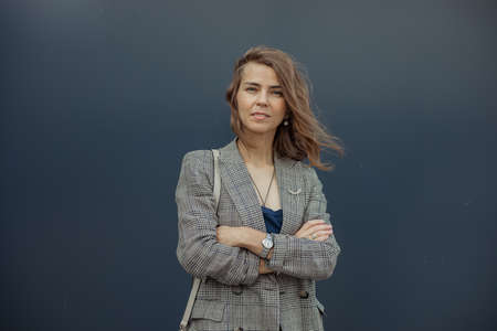 Portrait of elegant young businesswoman standing with crossed arms in stylish blazer and squinting on gray background. Urban lifestyle, entrepreneur, well dressed lady, successful peopleの写真素材