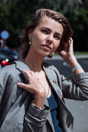Portrait closeup of pretty young businesswoman with nice makeup walking on street on sunny day and fixing hair. Urban lifestyle, roadway, sun shining, thoughtful lady, successful peopleの写真素材