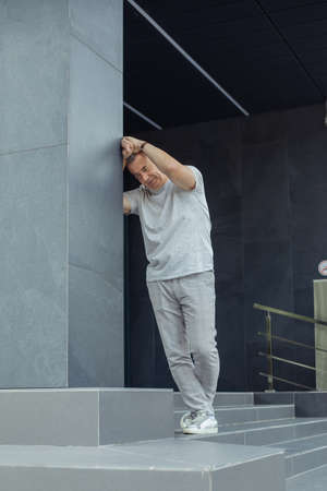 Portrait of worried aged businessman leaning on gray construction of modern office building with...