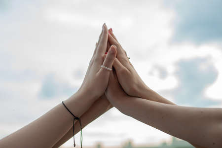 Cropped photo of young women folding hands, giving high five, clapping on sky background. Symbol of unity, friendship.の写真素材