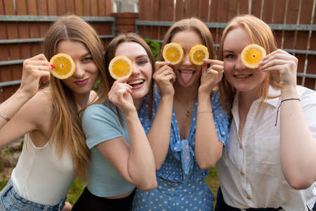 Portrait of young laughing women raising hands to face, covering eyes with slices of orange, having fun, joking.の写真素材