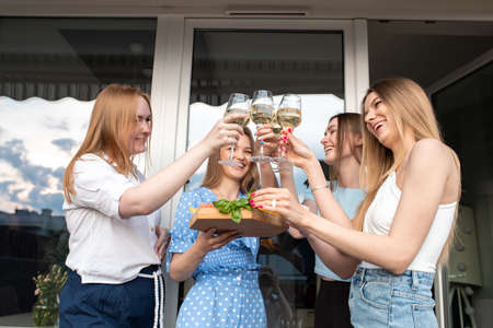 Portrait of young happy good-looking women holding vegetables, clinking glasses of white wine,...
