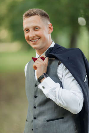 Vertical portrait of confident, cheerful, smiling blond businessman or groom in formal wear with watch holding jacketの写真素材