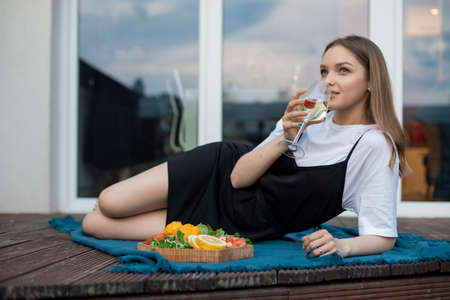 Portrait of young woman lying on blue blanket near cut fruits, vegetables, greens on tray, drinking...