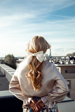 Rearview vertical blond fashionable woman in sunglasses and silk dress on rooftop posing, looking at city. Copy spaceの写真素材