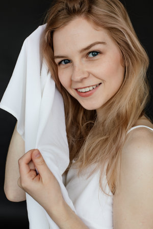 Vertical portrait of positive, smiling, glad and delightful blonde woman look at camera and drying wet hair with towelの写真素材