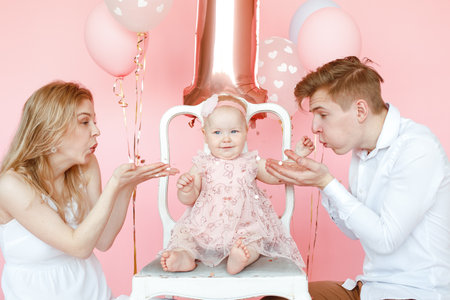 Small little smiling, glad barefoot one year toddler infant child in pink dress sitting on chair on...