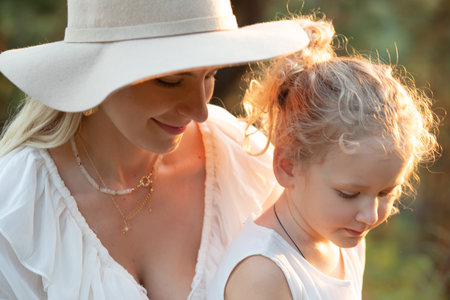 Portrait of loving family wearing white dresses, sitting near trees in forest lit up by sunset in...