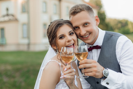 Cheerful, laughing married couple of bride in wedding dress and groom in suit drinking and toasting...