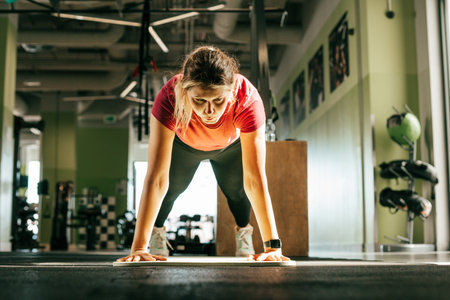 Plus size girl stand on outstretched arms and legs looking down in fitness gym. Young woman pump up...
