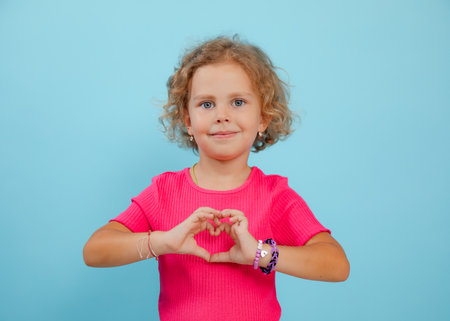 Small expressive, confident, playful, positive curly blonde girl showing heart sign by hands. Love...