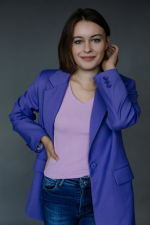 Portrait of beautiful young woman in stylish blue female blazer touching hair on gray background, free copy space. New collection of basic casual clothes, bright office outfit, working lifestyleの写真素材