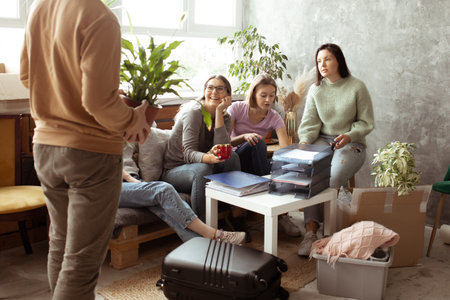 Positive laughing talk female students meeting together to help packing luggage stuff. University or...