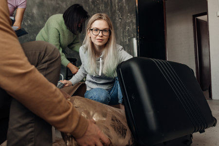 Busy woman in glasses with friends pack luggage suitcase and try to fit things in living room....