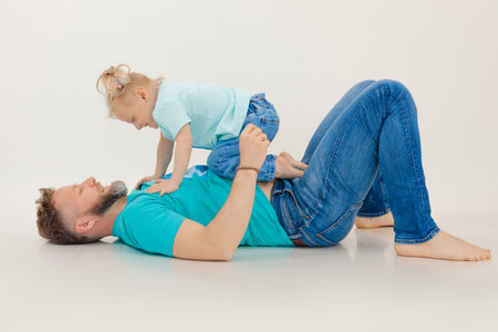 Portrait of family wearing blue T-shirts, jeans. Little smiling girl with short fair hair standing on all fours on man.の写真素材