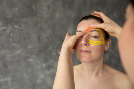 Cropped photo of therapist doctor woman applying orange yellow tapes on forehead of middle-aged...