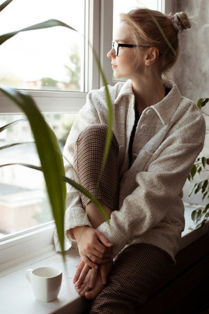 Vertical dreaming, tranquil, thoughtful blond woman in glasses and warm sweater sitting on...