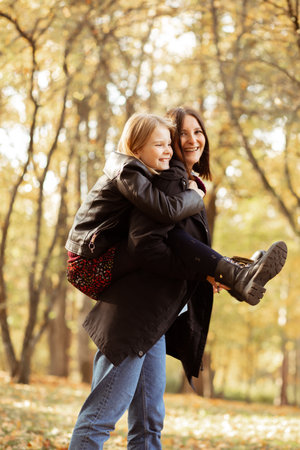Rejoicing young woman ride on back little girl side view. Happy mother and daughter in casual black...