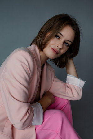 Portrait of beautiful business woman in stylish pink female pantsuit posing on gray wall, free copy space. Glamour fashion style collection of new casual season clothes for young ladiesの写真素材