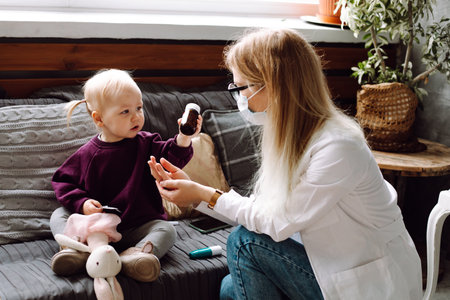 Portrait of wonderful little girl sitting on sofa, giving brown bottle to childrens doctor playing...