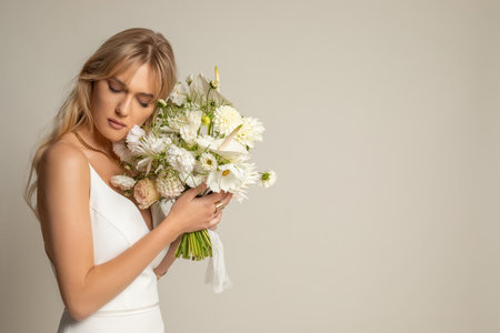 Gentle, calm dreamy elegant blond woman in white dress hold bouquet of flowers near face on white background. Copy spaceの写真素材