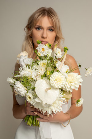 Vertical charming relaxed anticipating blond woman, bride in light white dress covered with big white bouquet of flowersの写真素材