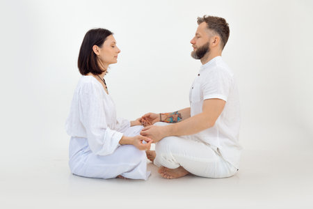 Tranquil sporty family of woman, man sitting with crossed legs, closed eyes on floor, meditating on white background.の写真素材
