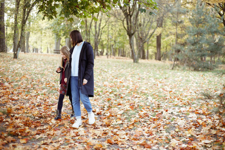 Merry, smiling family of mother and daughter strolling around in autumn forest. Travelling and have...