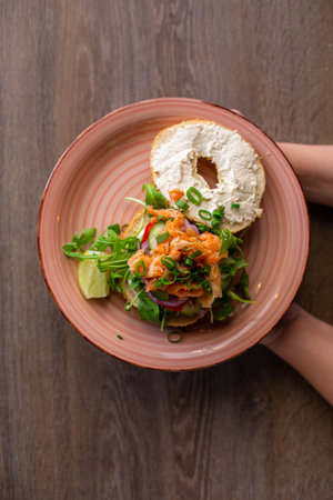 Vertical yummy donut burger buns with cream cheese and greenery, fish filling, sauce served up on pink plate. Top viewの写真素材