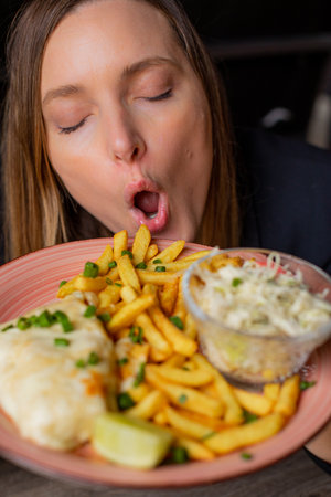 Young woman hold plate with fries, chicken fillet and vegetable salad and enjoy flavour with closed eyes and open mouth. Serving of main dish and garnish closeup. Love food, restaurant dish, dinnerの写真素材