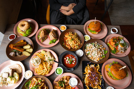 Top view photo of woman sitting at table full of delicious food in plates. Fries, soup, salad, burgers, sauces on festive dinner. Food, many dishes, menu of restaurant, beautiful serving foodの写真素材