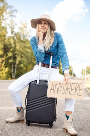Grimacing, waiting, independent blond woman in cowgirl hat hitchhike by road with plate anywhere sit...