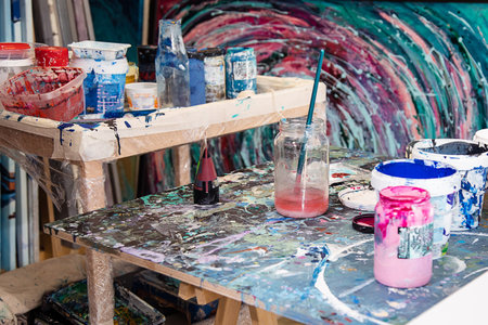 Interior of creative art workshop. Different buckets with paint, dirty glass jars, wooden desks stained with paint.の写真素材