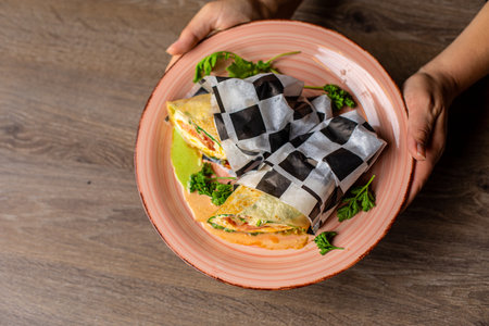 Cropped photo of woman holding big plate with burritos wrapped in checkered paper with vegetables...