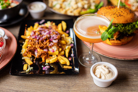Close-up of yummy dish from French fries and cut red onion on black plate near cocktail decorated with oranges. Food.の写真素材