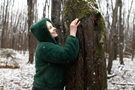 Happy woman in winter forest. Female portrait in snow park. Smiling woman in eco fur jacket touch...