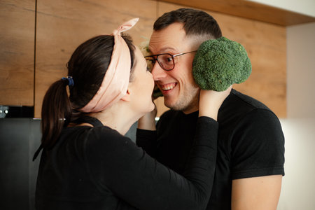 Woman hold green broccoli near male ears. Husband and wife have fun with love looking at each other....